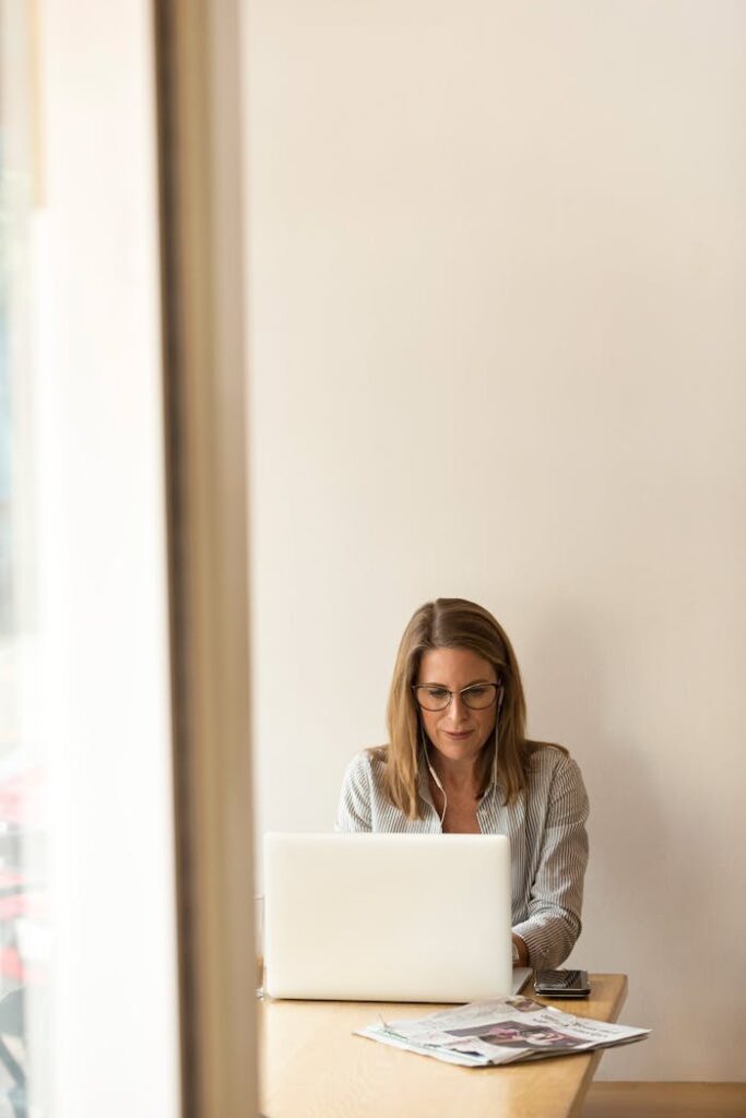 Businesswoman working remotely on a laptop at home, enjoying natural light in a modern, minimalist setting.